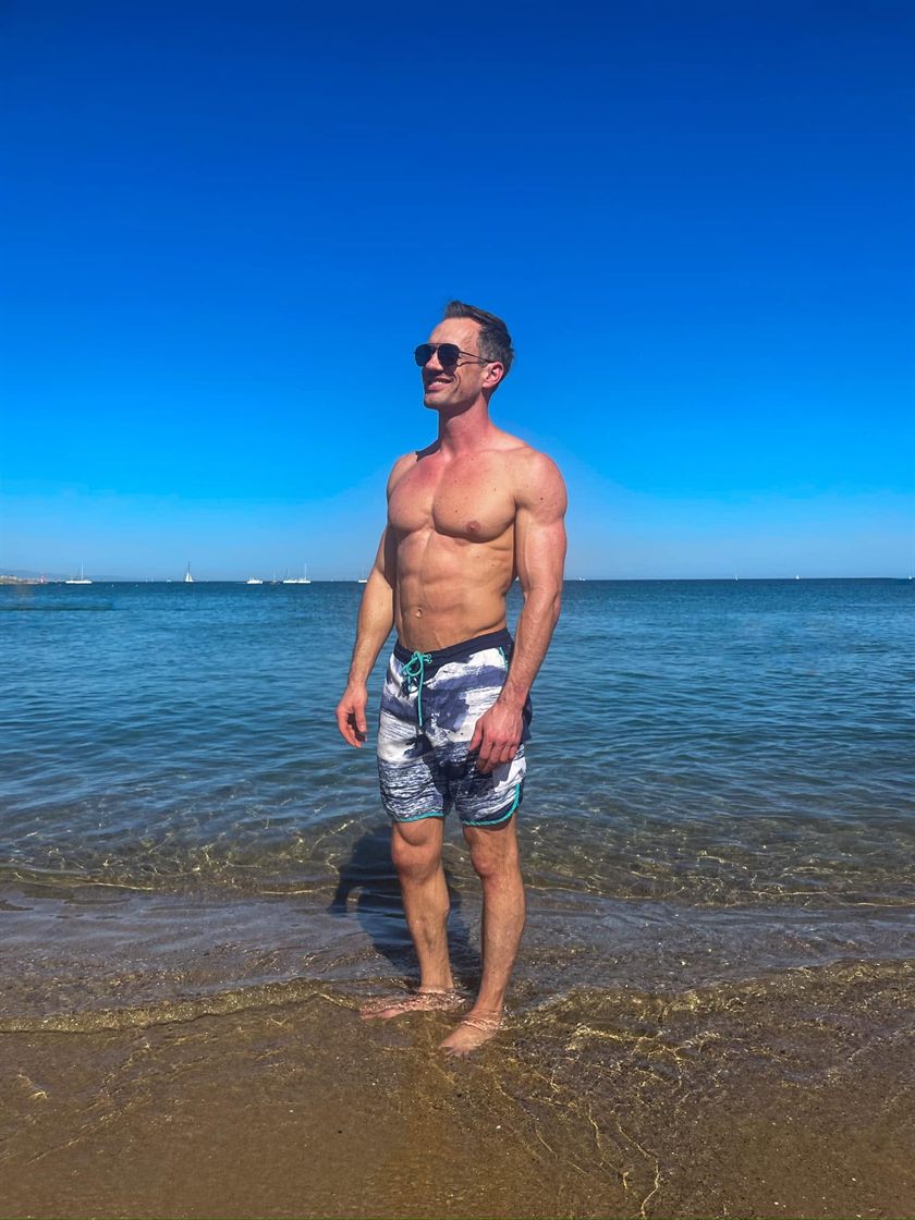 Taylor standing in clear shallow water at a beach on a bright day.