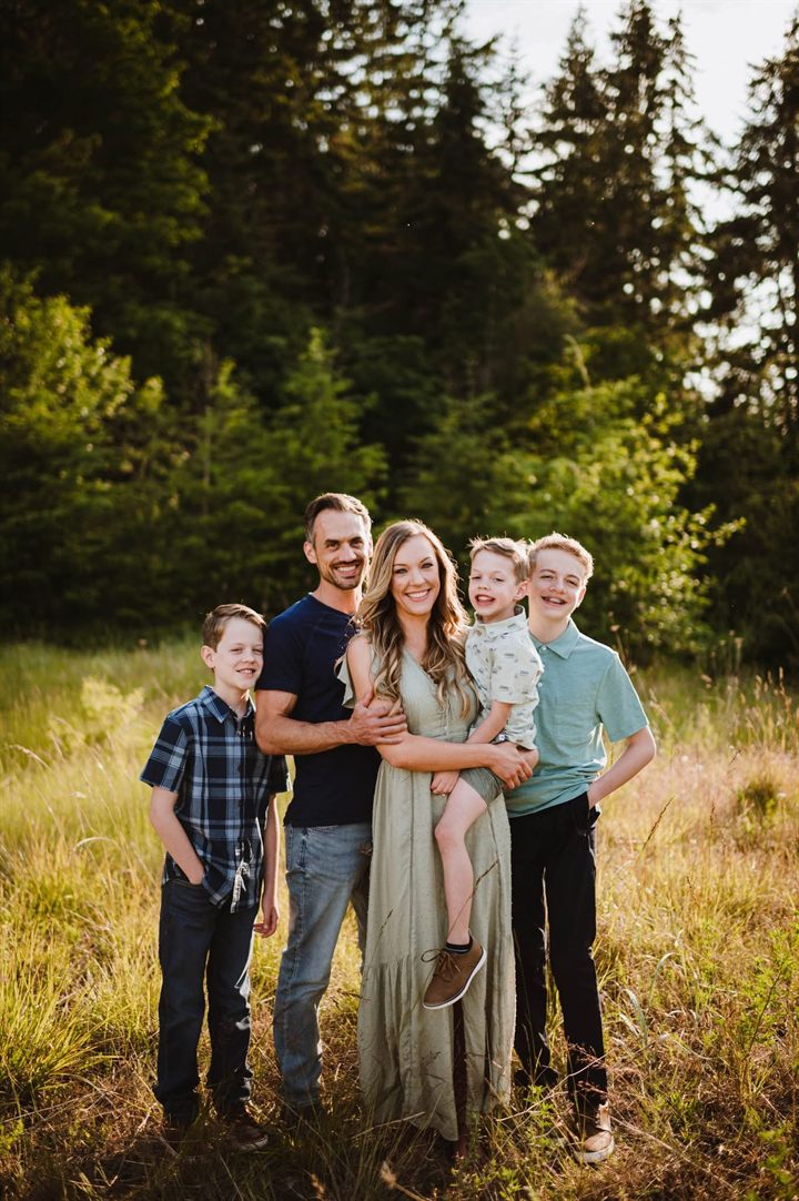Taylor with his wife and three sons in a grassy field in summer light.