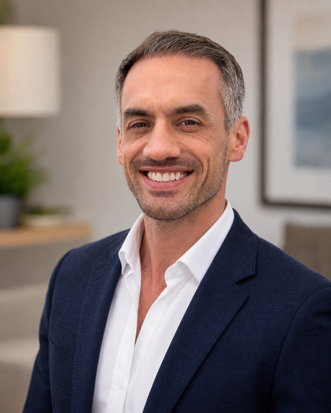 Taylor Bivens in a navy blazer and white shirt, smiling in a softly lit room.
