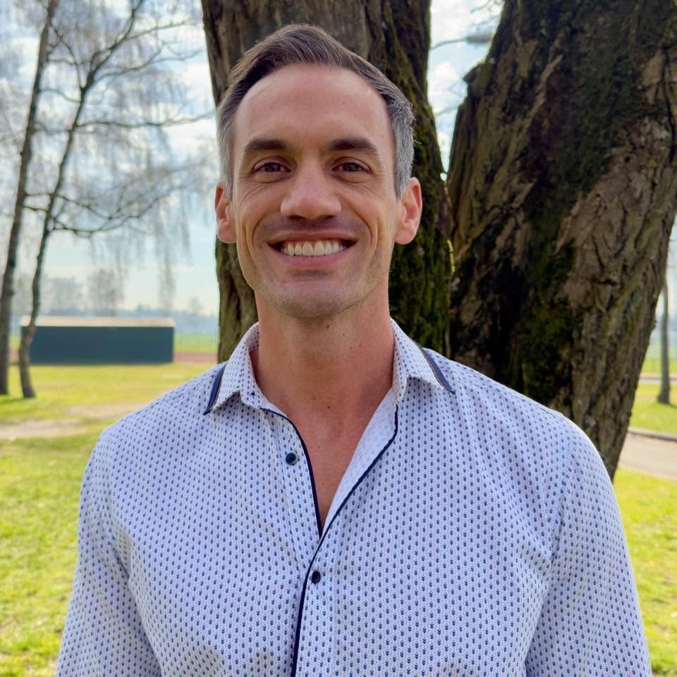 Taylor Bivens smiling in a light button-down shirt, outdoors in soft light.