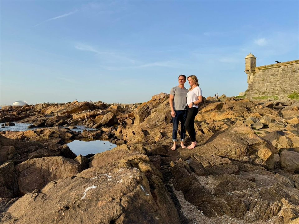 Taylor and his wife standing on the rocky coast at Porto, an old stone fort behind them.